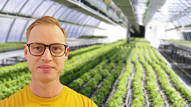 En person syns i närbild i förgrunden, i bakgrunden syns interiören i ett växthus.