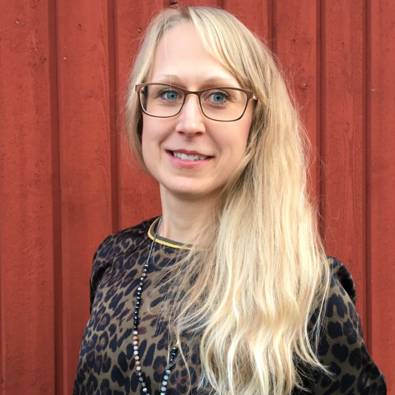 Anna Lindgren har blont hår och står mot en röd ladugårdsvägg