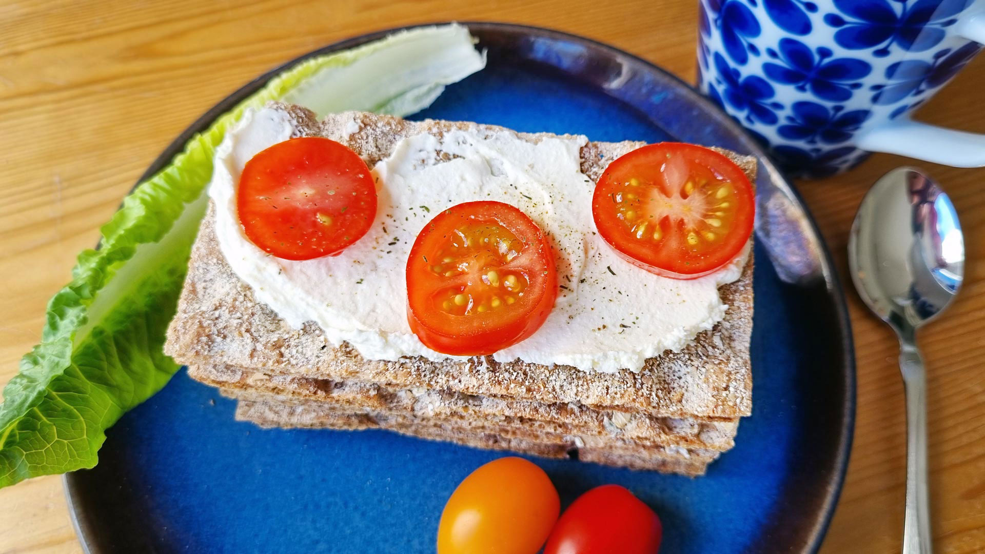 Knäckebröd på en blå tallrik, med färskost och tomater.