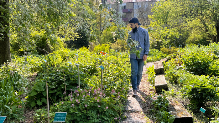 Taha Zouhair går bland olika plantor i en trägårdspark