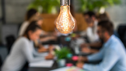 En glödlampa skiner starkt över ett bord med personer som ligger ur fokus