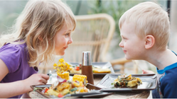Två barn äter mat vid ett bord utomhus