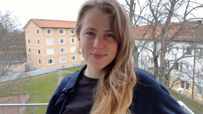 Sara Sjöqvist står på en balkong. Hon har långt brunt hår och en blå tröja.