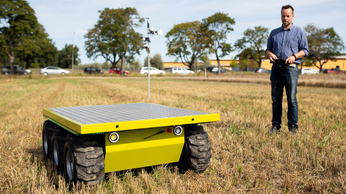 Jonas Engström Jadvi står på en stubbåker med en gul robot