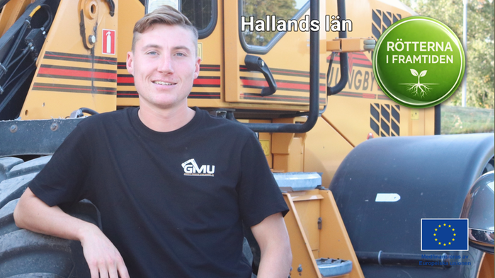 Henning Griph står vid sin gula traktor utomhus. Han har en svart t-shirt på sig. 