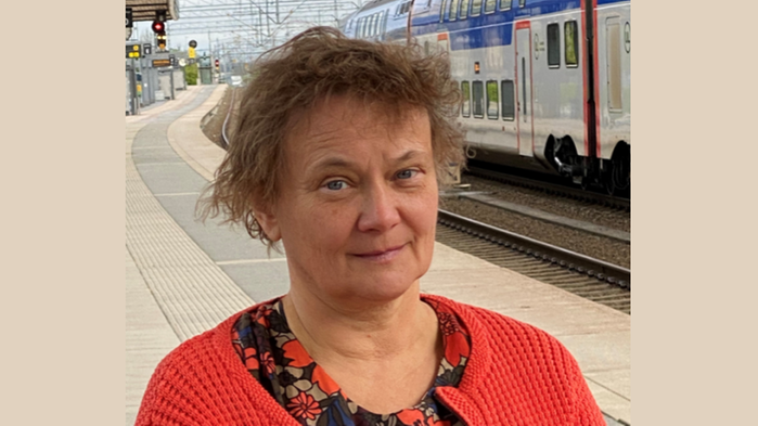 Helena Elmquist står på en perrong iförd röd kofta och med ett tåg i bakgrunden